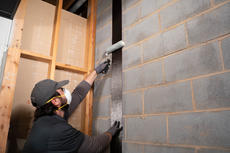 JES Foundation Repair crew member wearing face mask and gloves installing carbon fiber strap to a block basement foundation wall using a roller