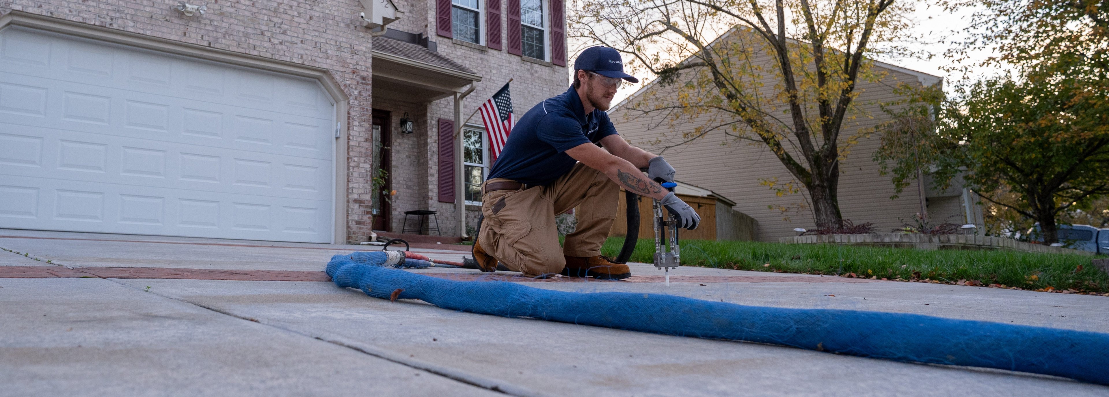 Groundworks technician injecting polyurethane foam to lift concrete driveway.
