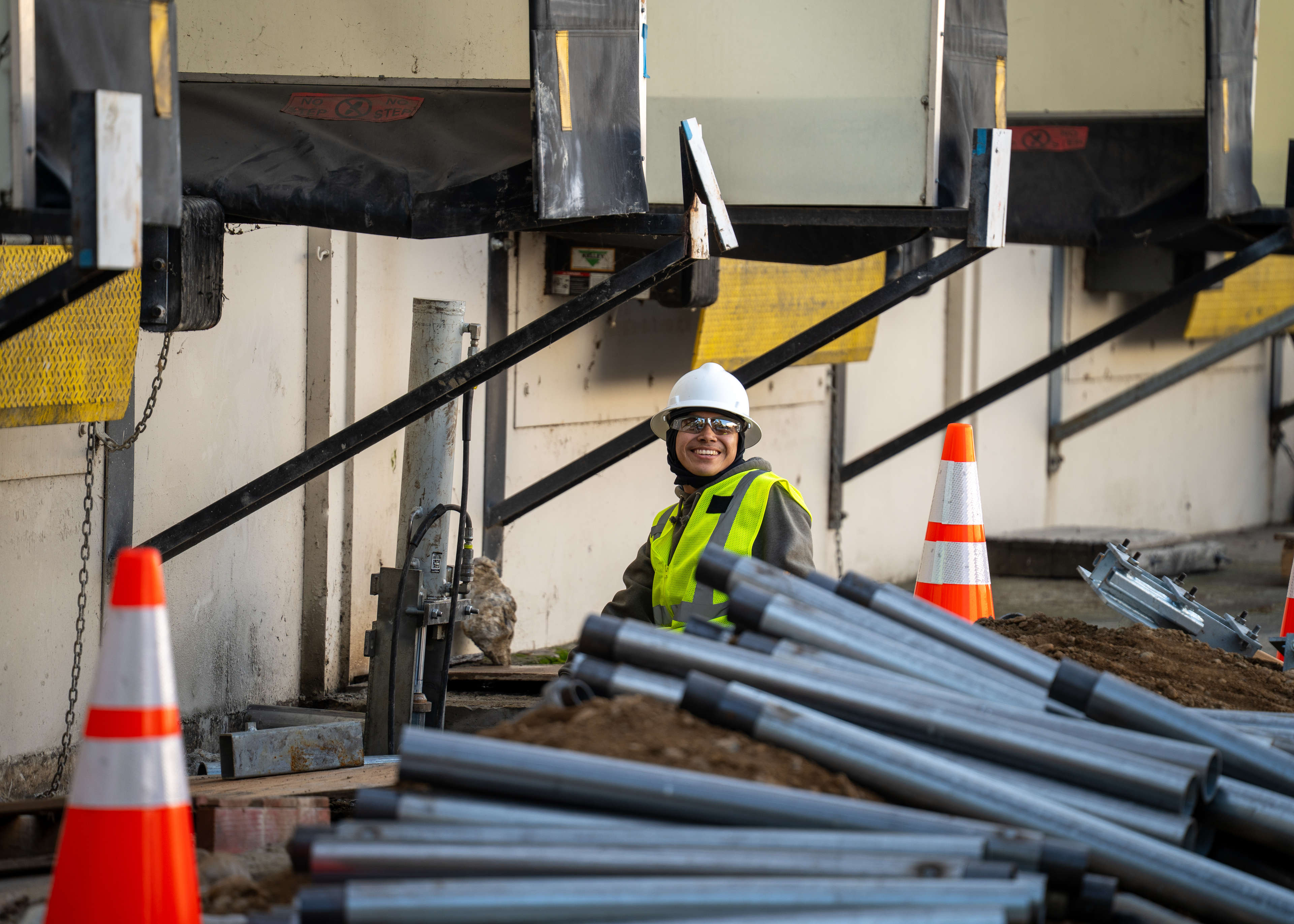 smiling crew member stands among sections of push piers during a commercial foundation repair project
