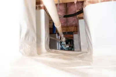 A crawl space with plastic lining, exposed beams, and HVAC ducts benefits from crawl space encapsulation, ensuring enhanced protection and efficiency.