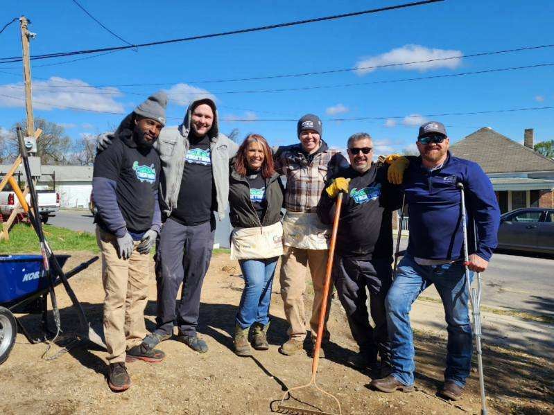 Six JES Foundation Repair members in outdoor work clothes posing together in a sunny, open area.