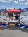 Outdoor booth with banners about basement and foundation solutions, staffed by a person under a red canopy.