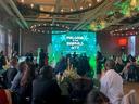A formal sponsorship event with JES Foundation Repair team members seated at tables, featuring a large screen that reads "Welcome to the Emerald City Kaleidoscope Ball.