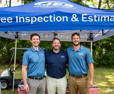 Three men in blue shirts stand under a tent offering free inspections and estimates.