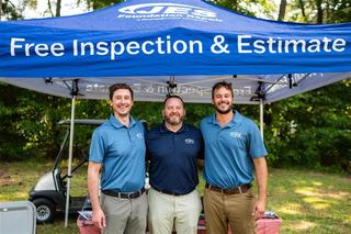 Three men in blue shirts stand under a tent offering free inspections and estimates.
