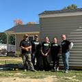 Five JES foundation Repair team members standing outside, smiling, in front of a light-colored shed on a sunny day.