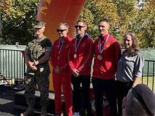 Five people pose outdoors, three in red tracksuits with medals, beside a marine and a woman, at an awards event.