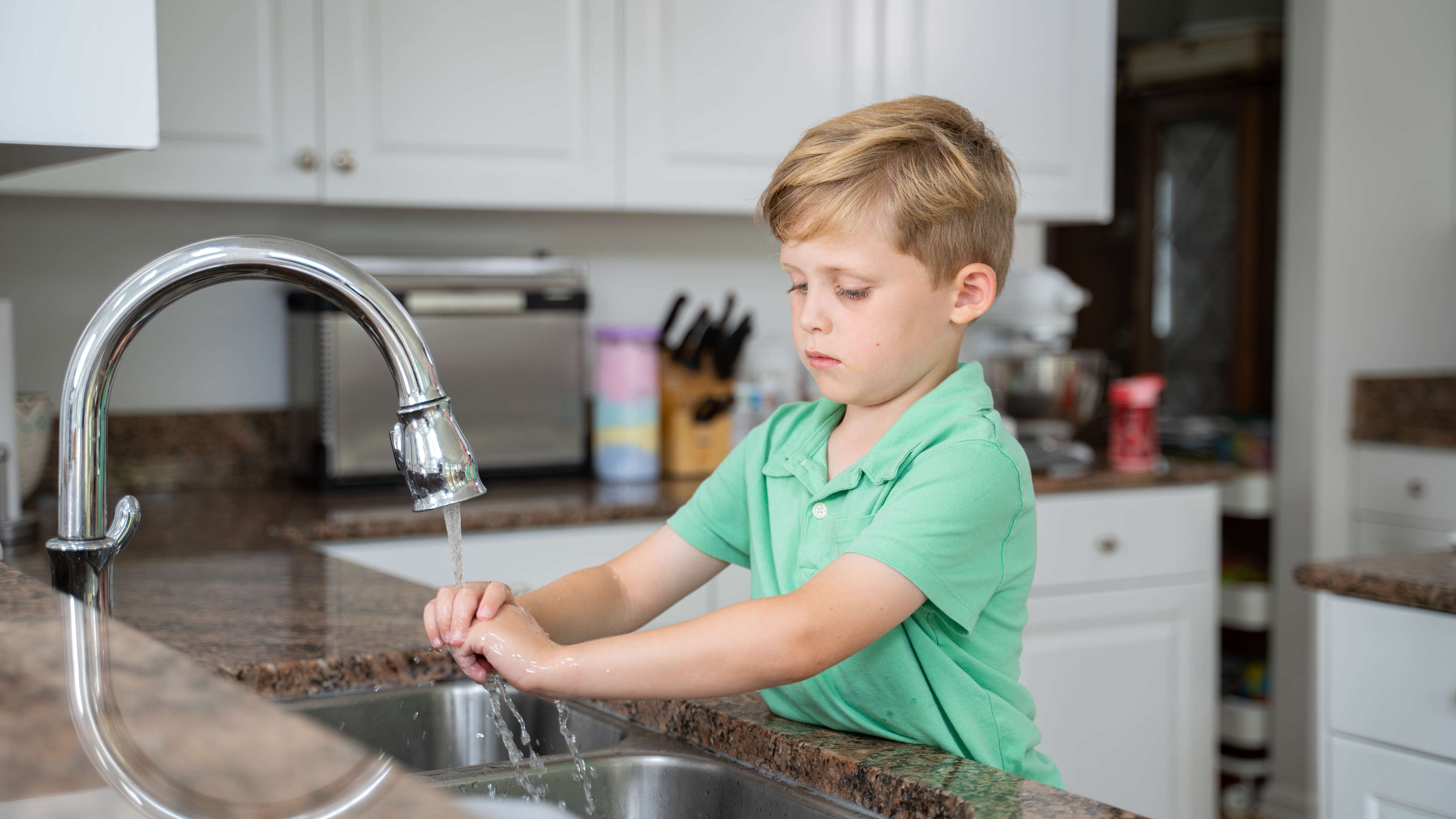 boy washing hands in kitchen sink