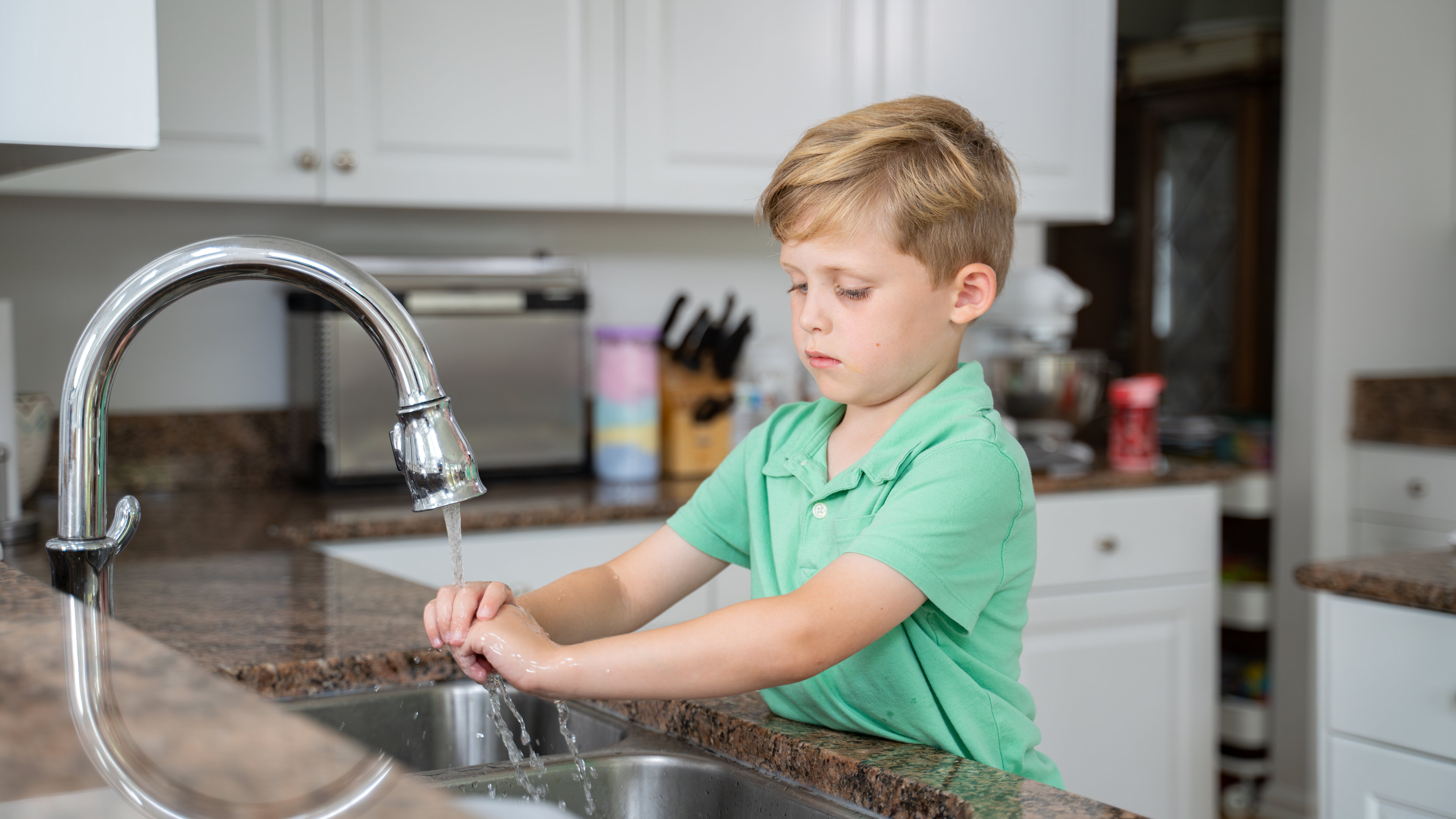 boy washing hands in kitchen sink