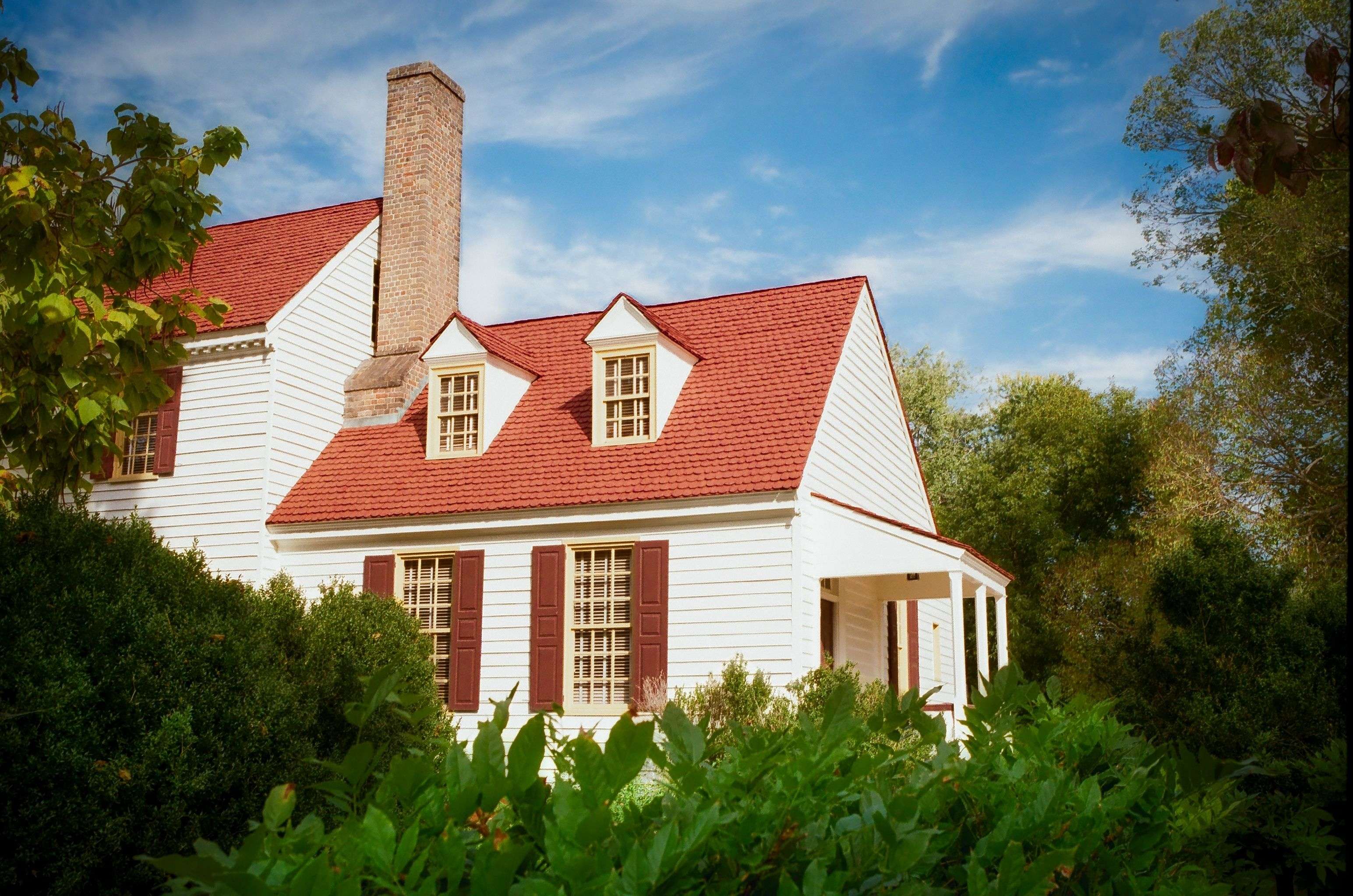 White two-story house with a brick chimney and red window shutters and roof.