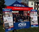 Five people stand at a JES Foundation Repair booth with banners and a red tent at an outdoor event.