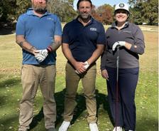 Three people in golf attire standing on a sunny golf course, smiling at the camera.