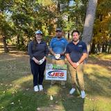 Three people stand on grass near a JES Foundation Repair sign, surrounded by trees on a sunny day.