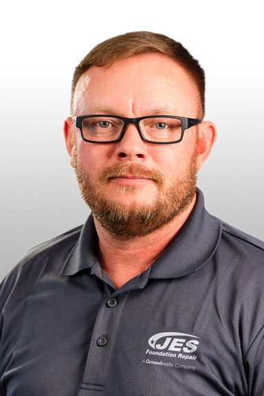 Man with short hair, beard, and glasses wearing a gray JES Foundation Repair polo shirt, facing forward.