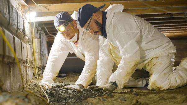 Mike Rowe assists a crew member during a crawl space repair project