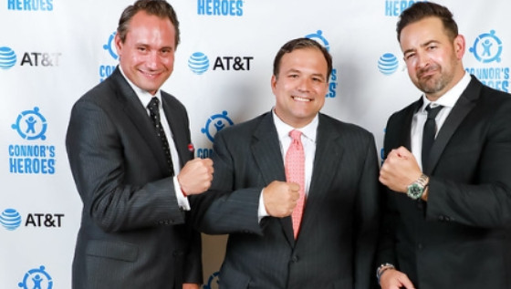 Three men in suits smiling and posing with fists raised in front of a Connor’s Heroes and AT&T backdrop.