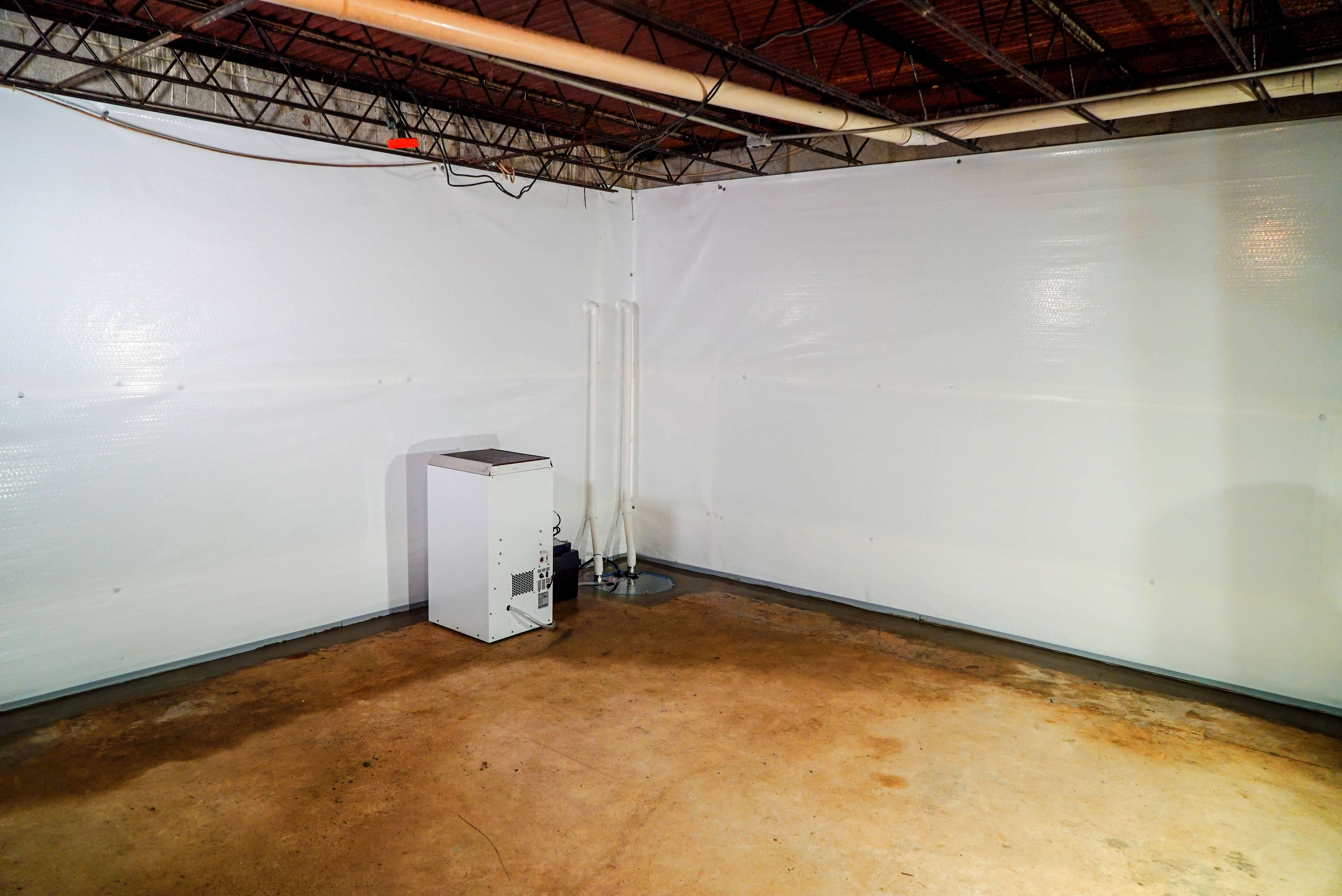 Basement with white plastic-covered walls, concrete floor, and a small dehumidifier in the corner.