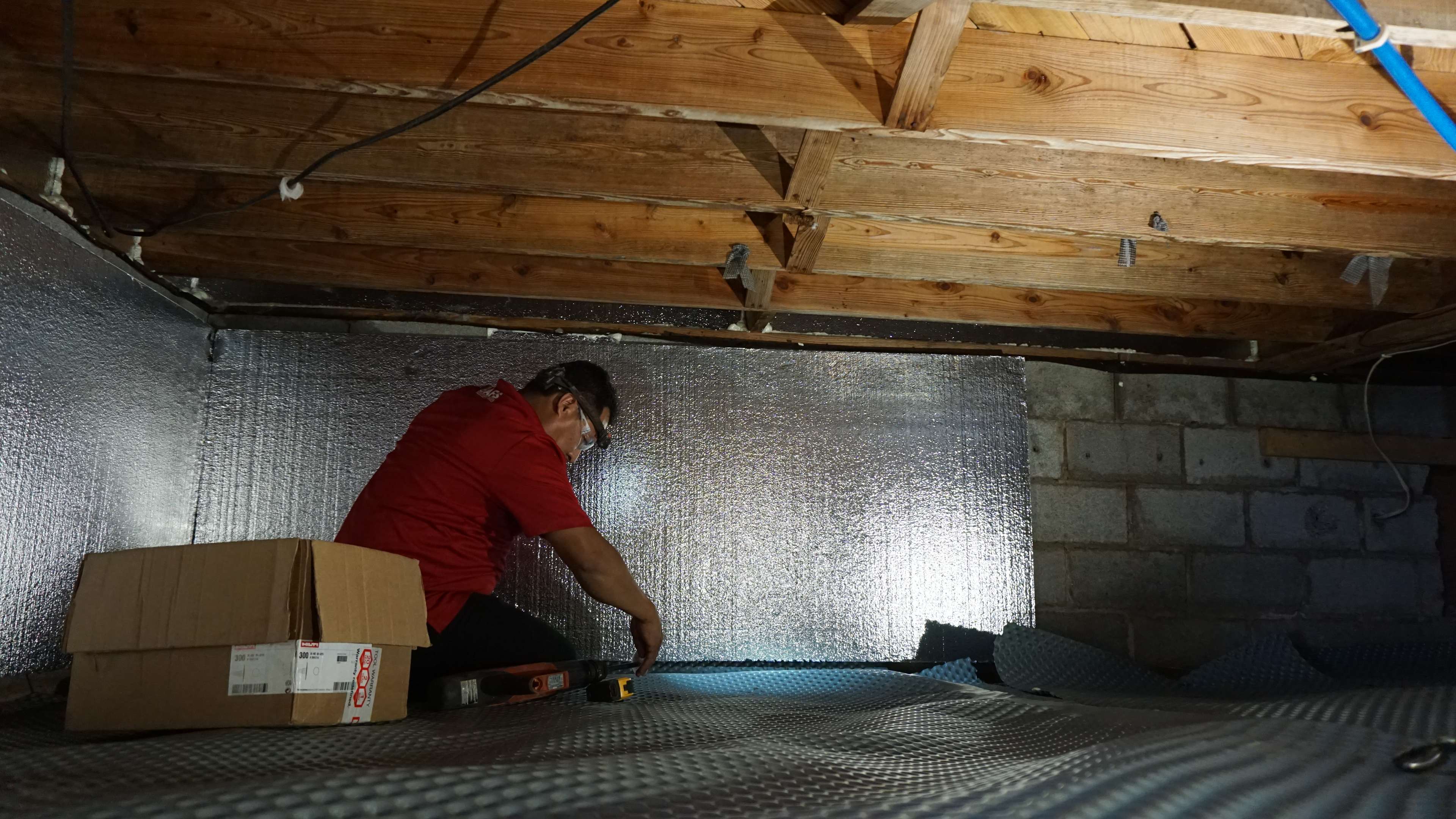 crew member installs crawl space insulation on walls in a crawl space