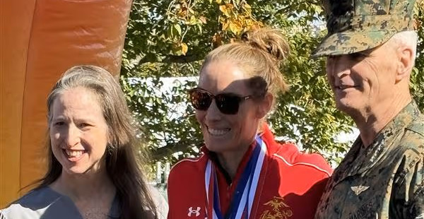 Three adults smiling outdoors; one wears military uniform, one has medals, and one has long gray hair.