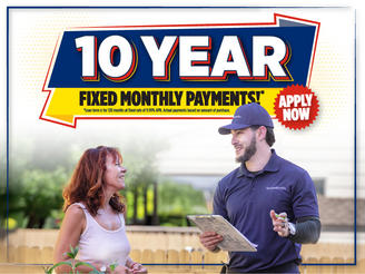 A woman discusses financing with a man in uniform holding a clipboard; sign says "10 Year Fixed Monthly Payments! Apply Now.