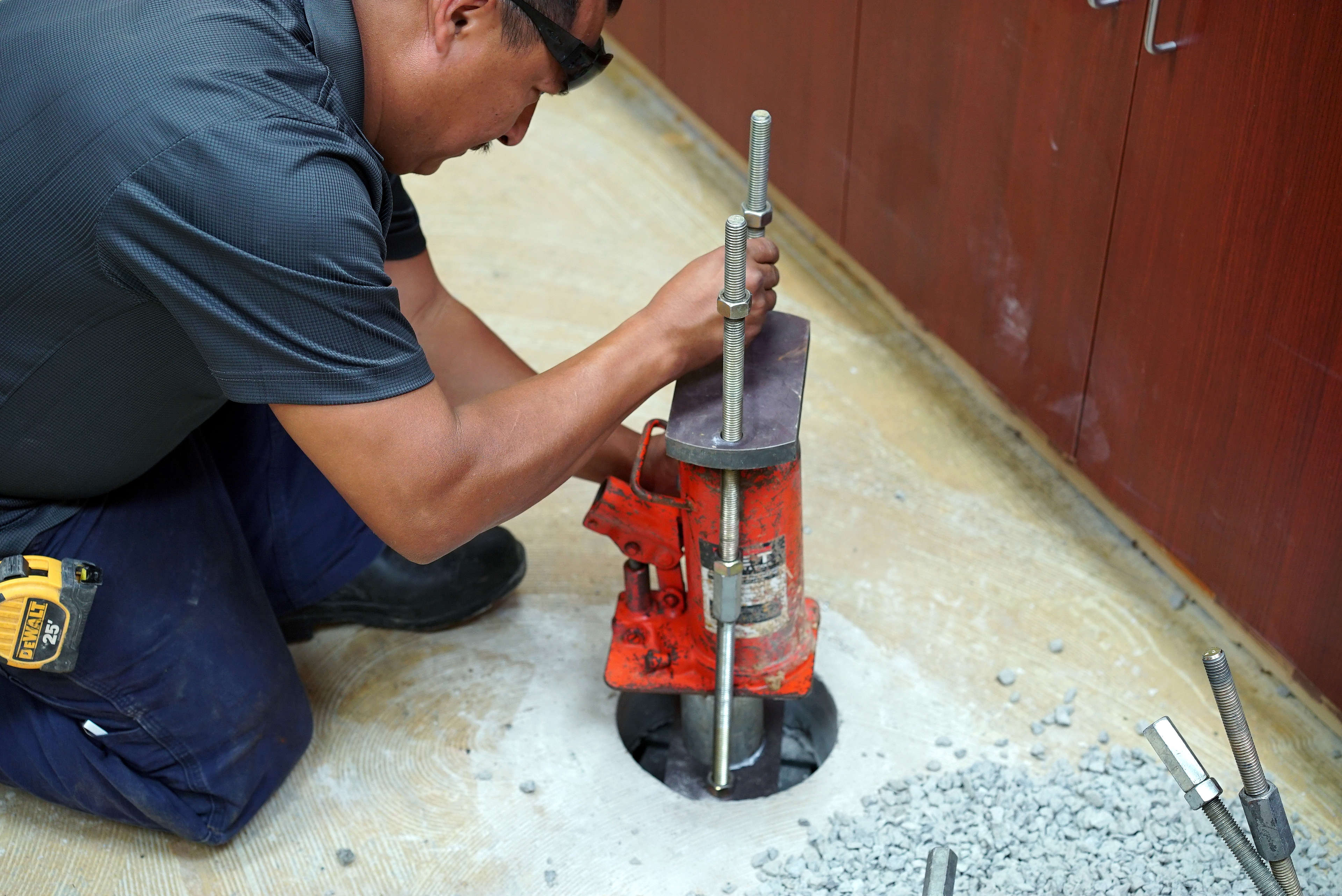 A person installs a metal slab pier into a hole in the concrete floor indoors.