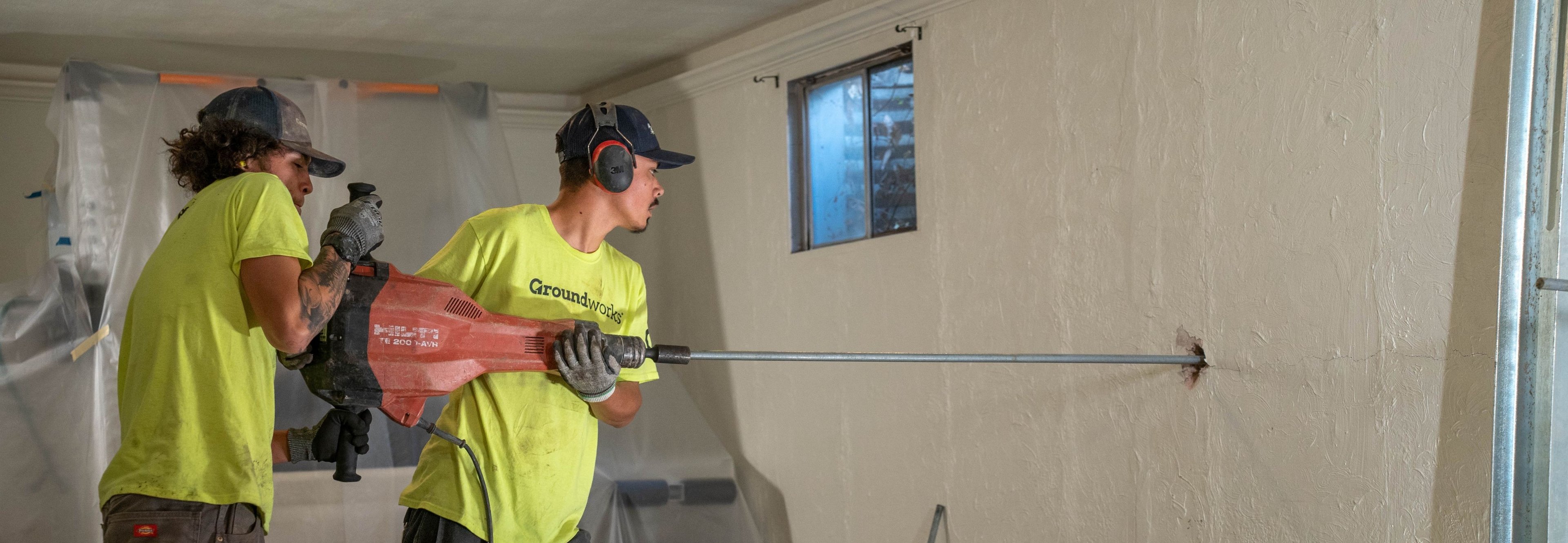 crew members drill a hole into a basement wall for wall anchor installation