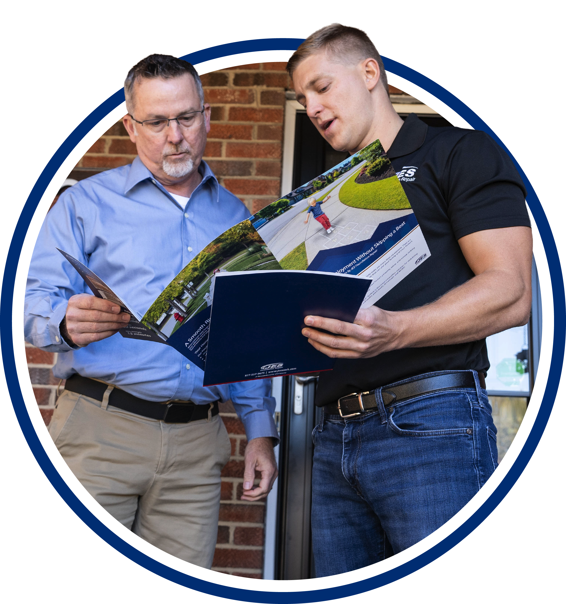 Two men stand outside, looking at brochures together, one wearing a blue shirt and the other in a black polo.