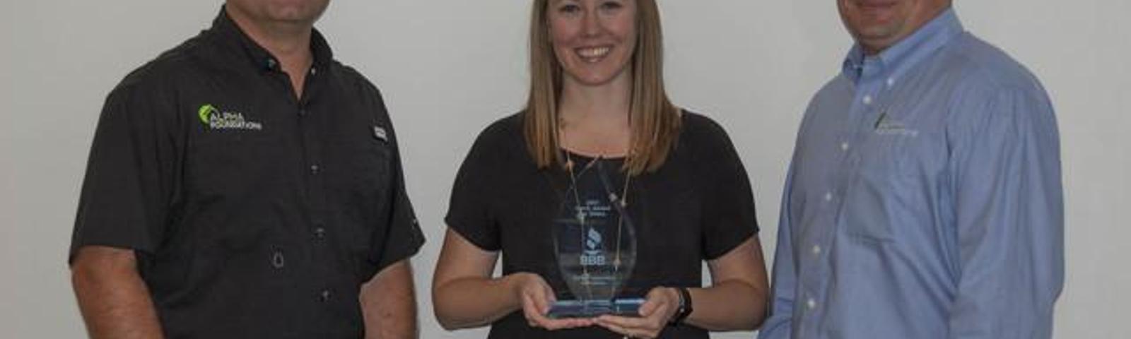 Three people standing, smiling, with one woman holding an award.