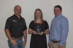 Three people standing, smiling, with one woman holding an award.