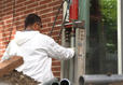 A person in protective gear operates construction equipment near a brick wall.