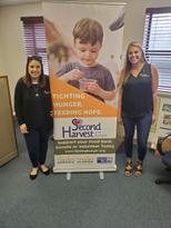 Two women standing next to a Second Harvest sign