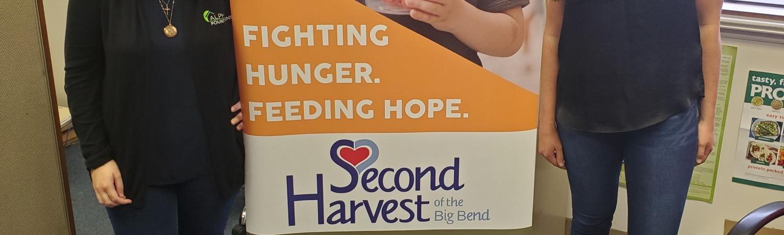 Two women standing next to a Second Harvest sign