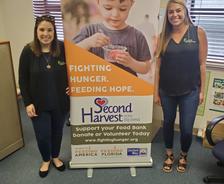 Two women standing next to a Second Harvest sign