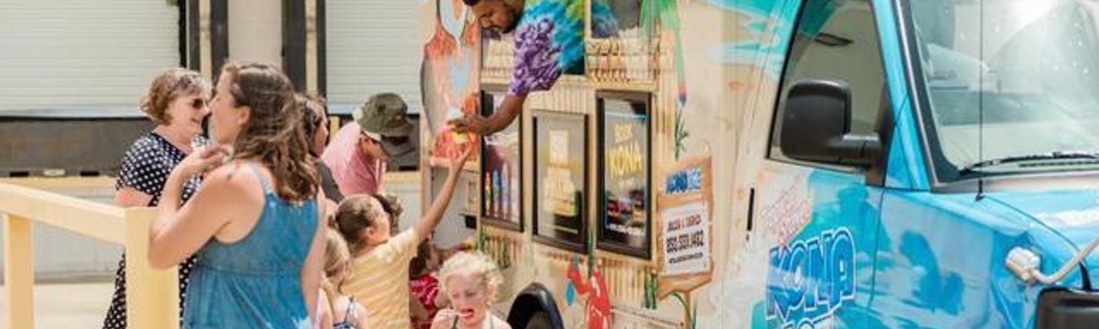 People ordering from a colorful ice cream truck on a sunny day.