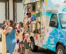 People ordering from a colorful ice cream truck on a sunny day.