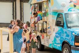 People ordering from a colorful ice cream truck on a sunny day.
