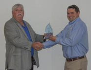 Two men shaking hands; one is holding a glass award.