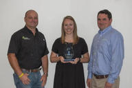 Three people standing, one holding an award, smiling against a plain background.