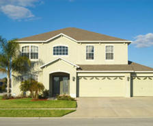 A two-story beige house with a three-car garage, palm tree, and clear blue sky.