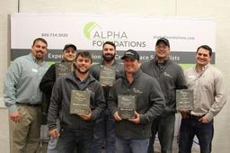 Seven people smiling, holding plaques, standing in front of an Alpha Foundations banner.
