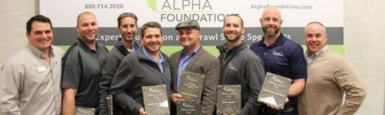 Seven men holding awards pose in front of an "Alpha Foundations" banner.