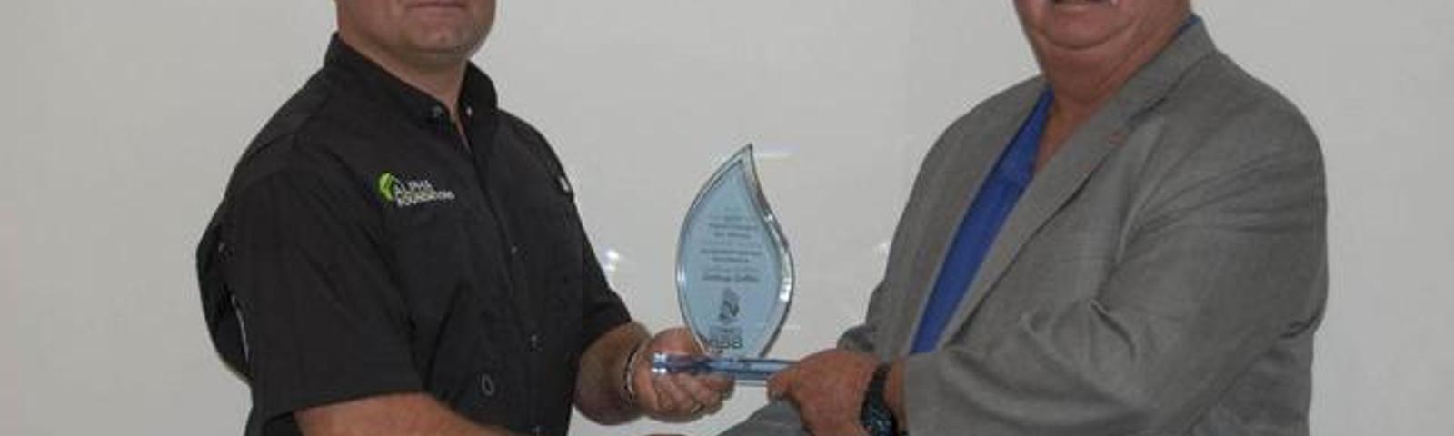 Two men shaking hands while one holds a glass award.