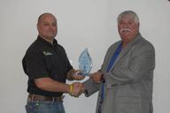 Two men shaking hands while one holds a glass award.