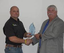 Two men shaking hands while one holds a glass award.