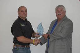Two men shaking hands while one holds a glass award.
