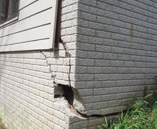 A house exterior with significant cracks and damage on a brick wall corner.