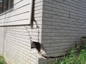 A house exterior with significant cracks and damage on a brick wall corner.