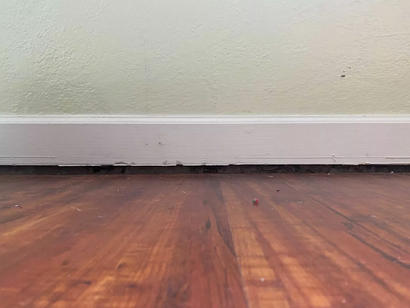 View of a wooden floor and baseboard with a noticeable gap, indicating structural separation.