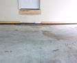 Concrete floor with a crack leading to a white door, showing signs of water damage.