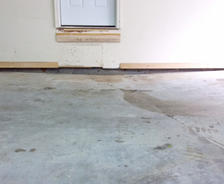 Concrete floor with a crack leading to a white door, showing signs of water damage.